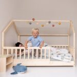 Kleinkind lachend mit Händen auf dem Geländer des Kinderbetts für Kleinkinder - Hausbett