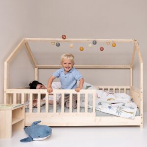 Kleinkind lachend mit Händen auf dem Geländer des Kinderbetts für Kleinkinder - Hausbett