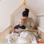 Gemeinsam ein Buch unter der Decke im Kinderbett für Kleinkinder lesen - Hausbett