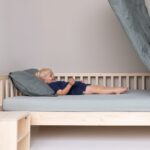 Kind lachend in Einzelbett Bettdecke in der Luft