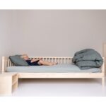 Im Kinderbett liegend und auf die Bettdecke zeigend