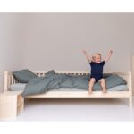 Auf der Kante des Kinderbettes sitzend und die Arme in die Luft gestreckt