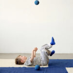 Junge liegt auf dem Boden und wirft einen MODU Foam Ball in Deep Blue und Sky Blue in die Luft