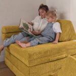 Gestapelte Elemente des ockergelben Jindl Cord Spielsofas beim gemeinsamen Lesen